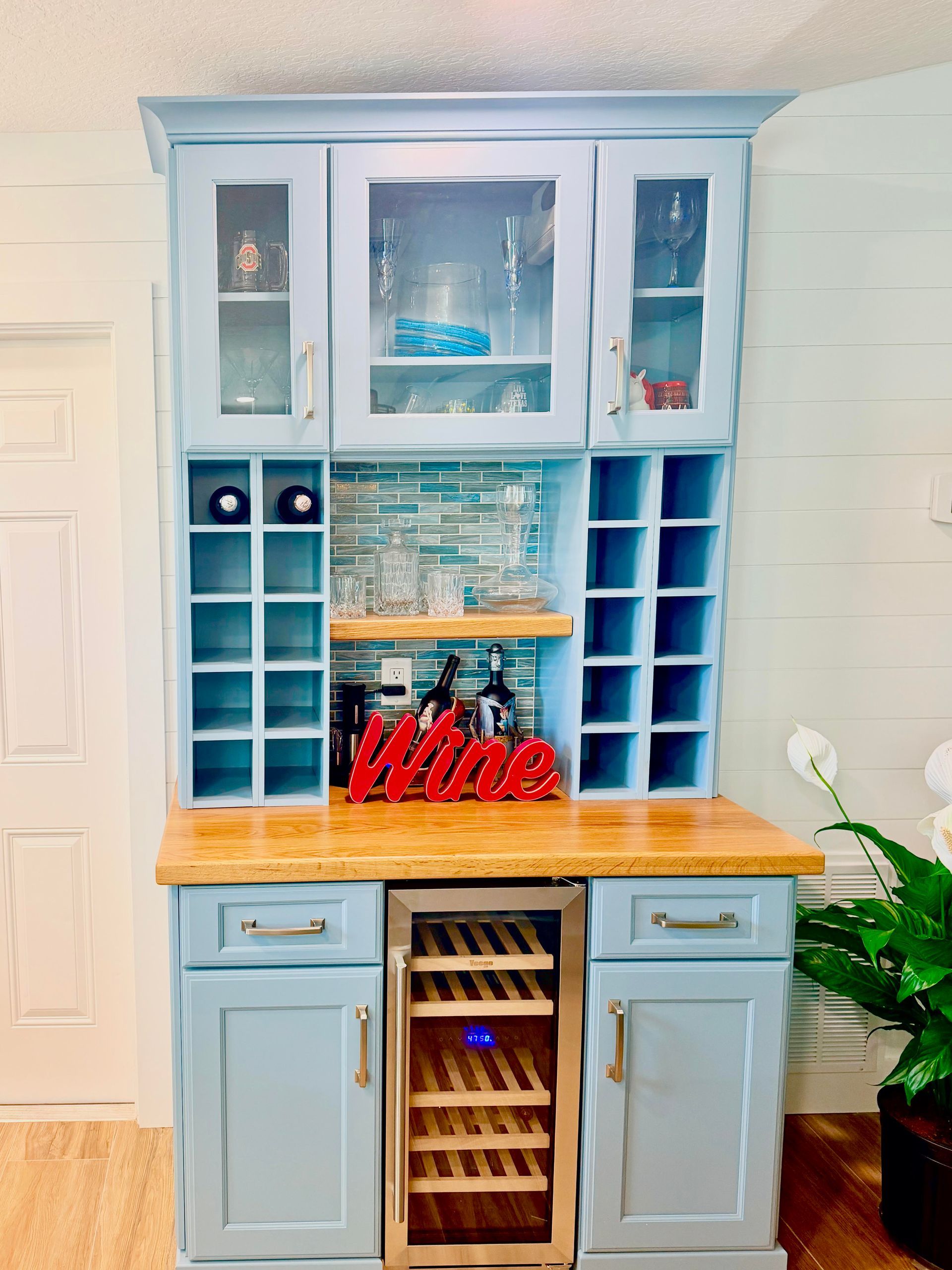 Blue hutch with wine storage and glasses, topped by a wooden counter in a bright kitchen nook.