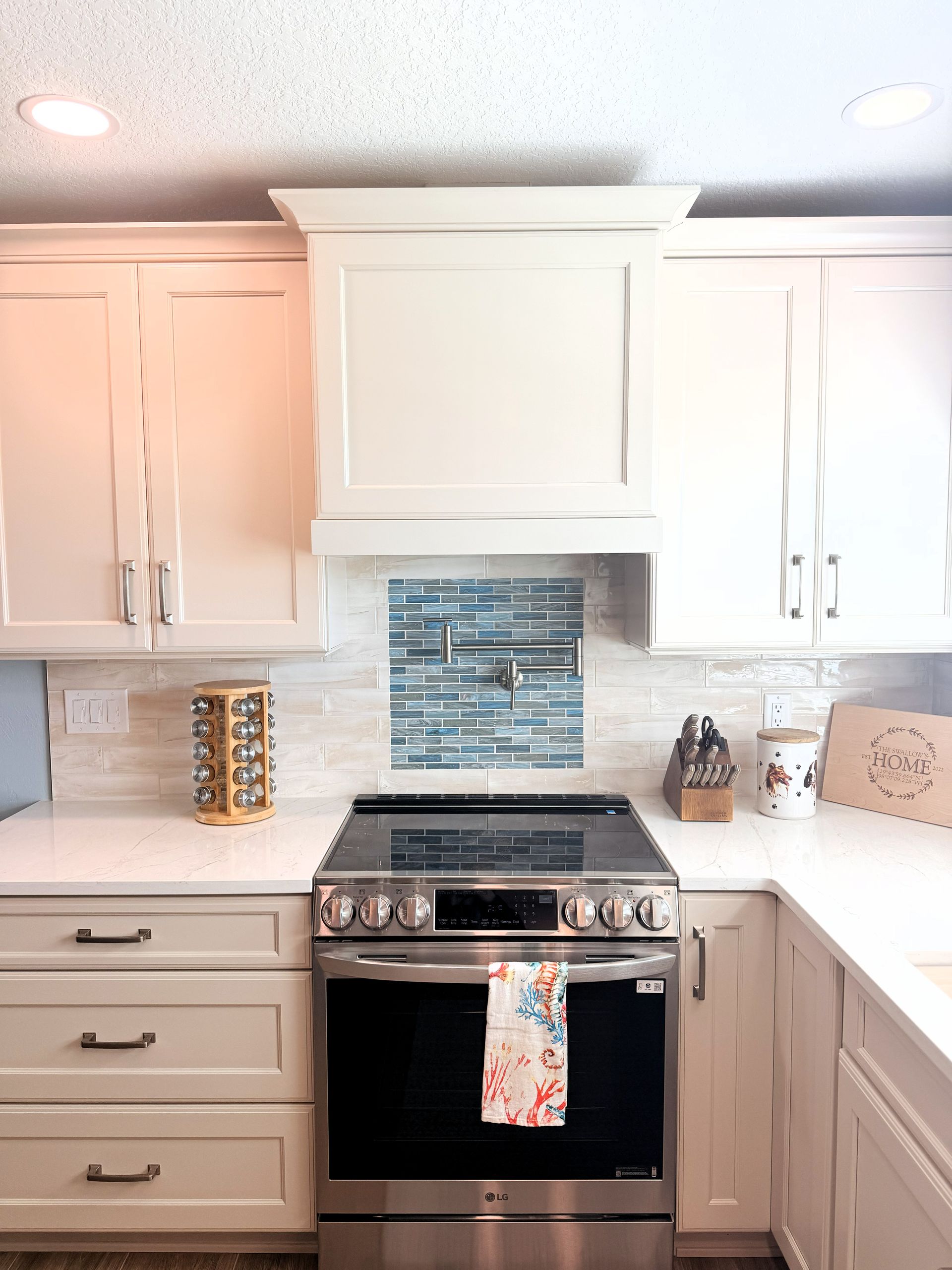 White kitchen with stainless stove, blue tile backsplash, marble counters, and white cabinets