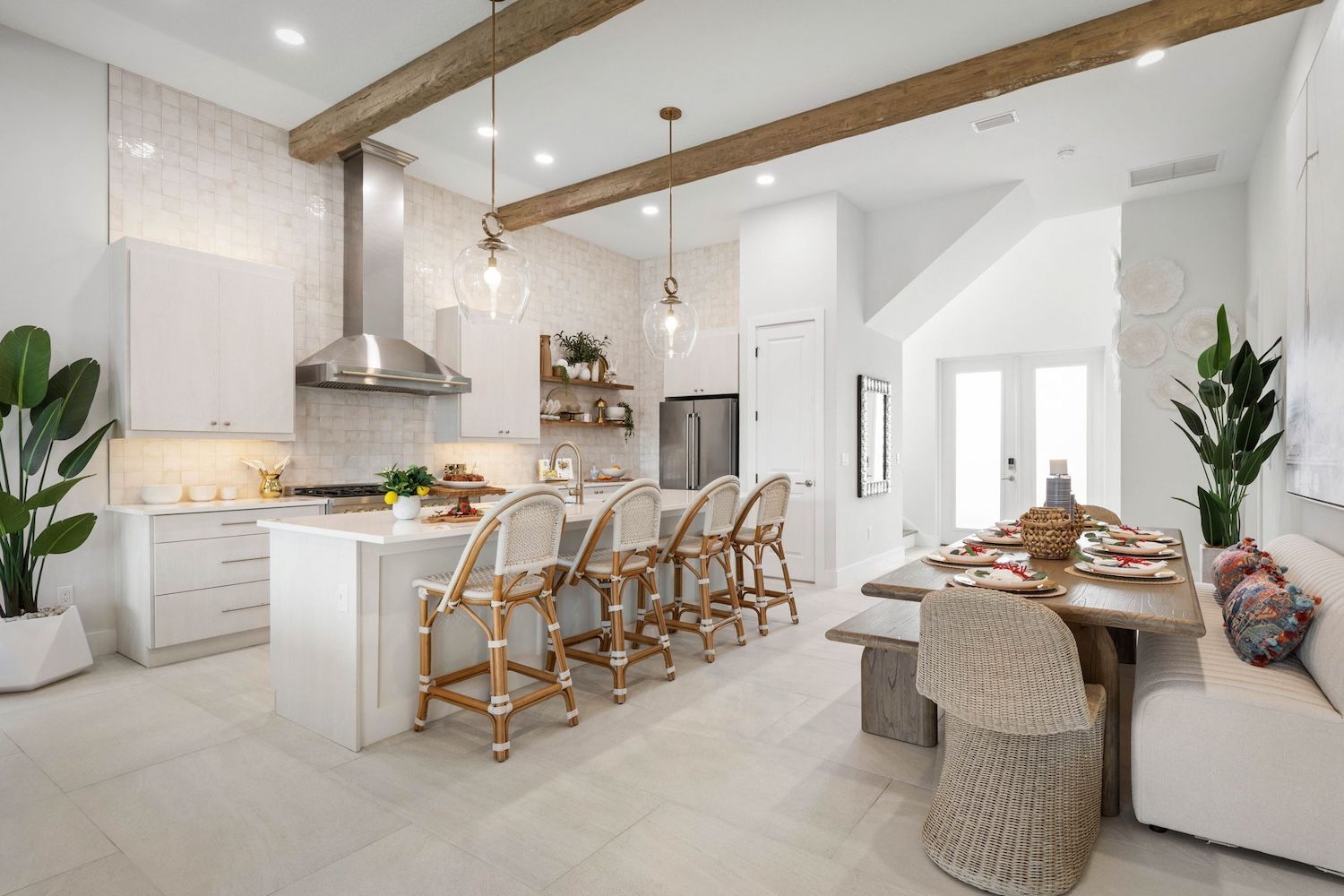 Bright modern white kitchen and dining area with rattan barstools, wood beams, and a set table