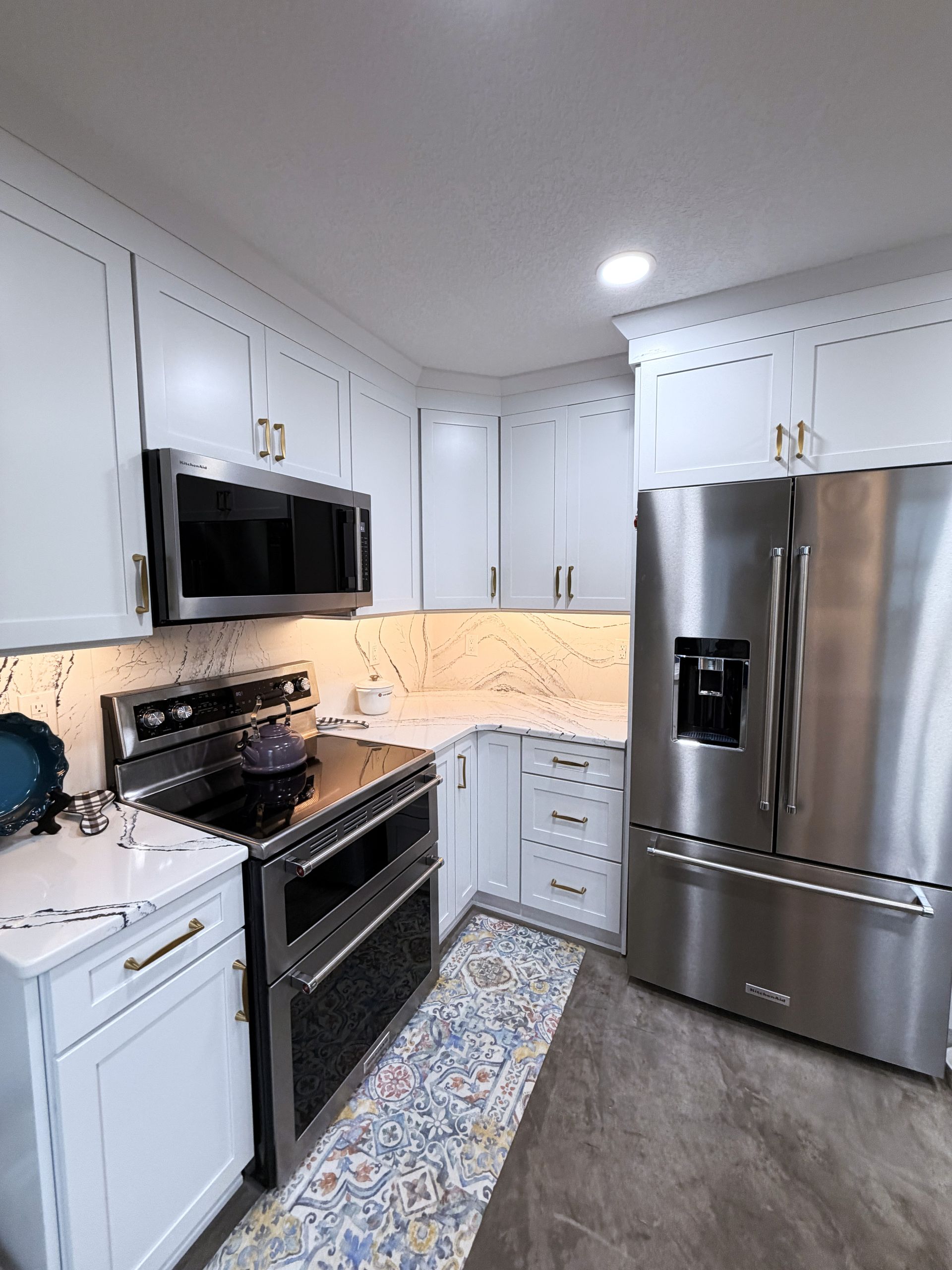 Bright white kitchen with stainless steel appliances, black stove, and patterned runner rug.