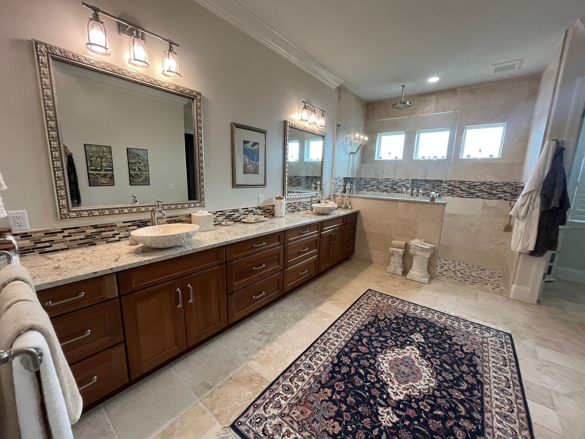Bright bathroom with double vanity, large mirror, tiled shower, and patterned rug