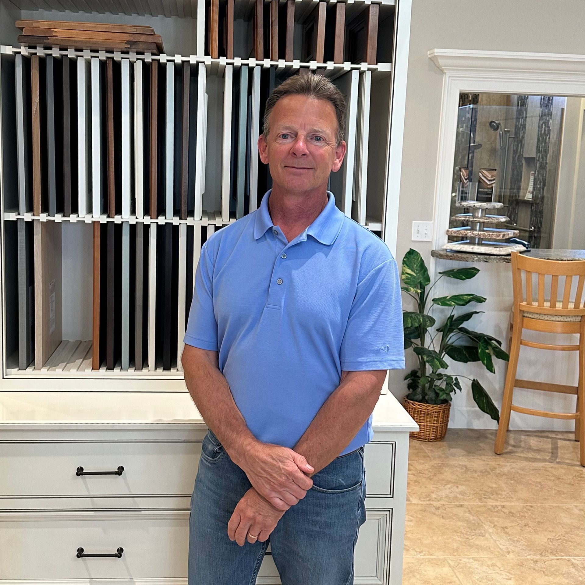Man in a blue polo shirt standing indoors beside a white cabinet with decorative screens behind him