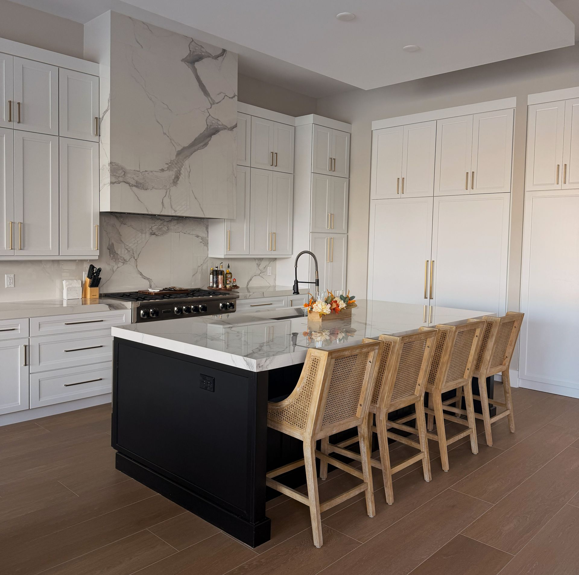 Bright modern kitchen with white cabinets, marble island, and four woven barstools
