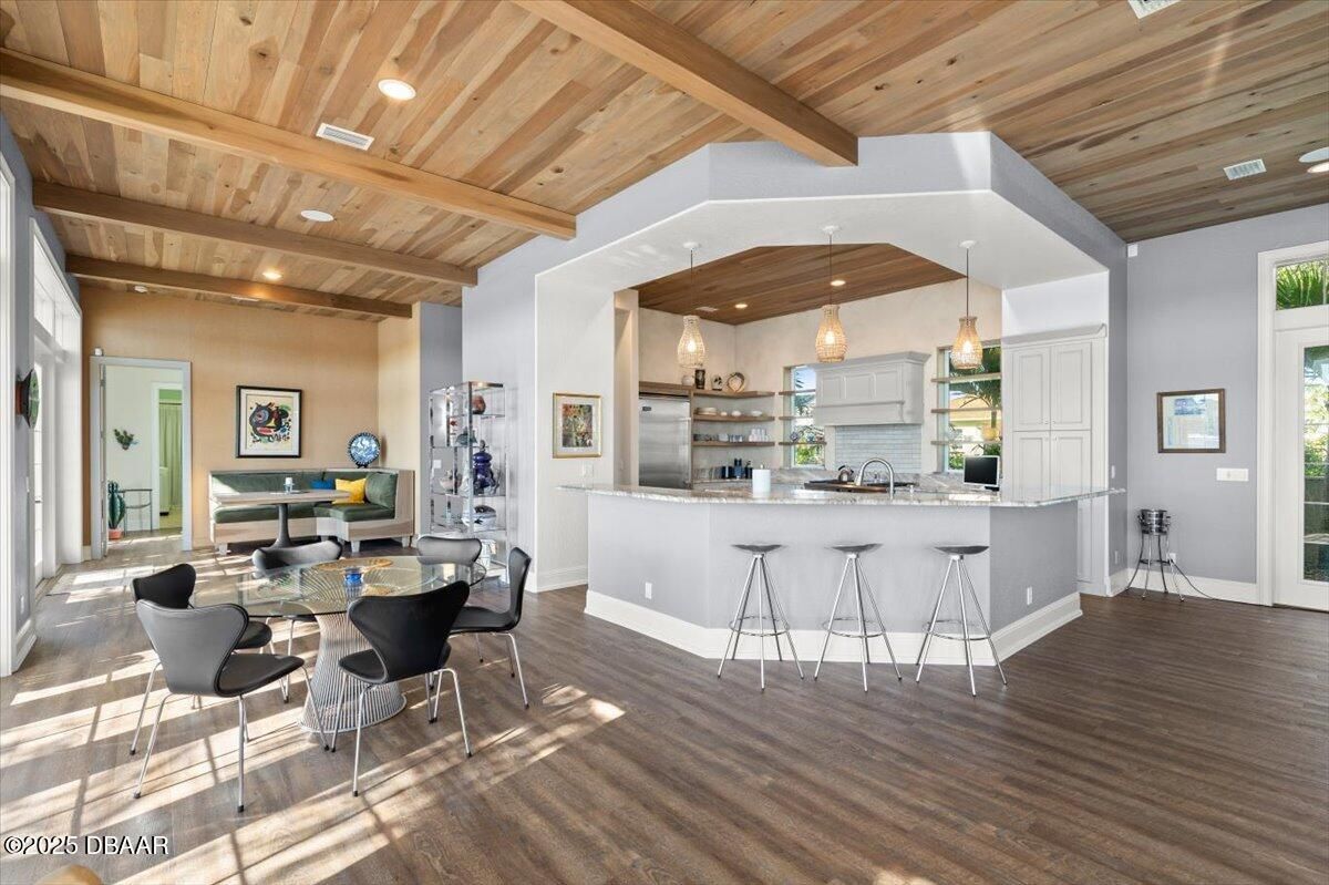Bright open kitchen and dining area with wood ceiling, bar stools, and dark flooring