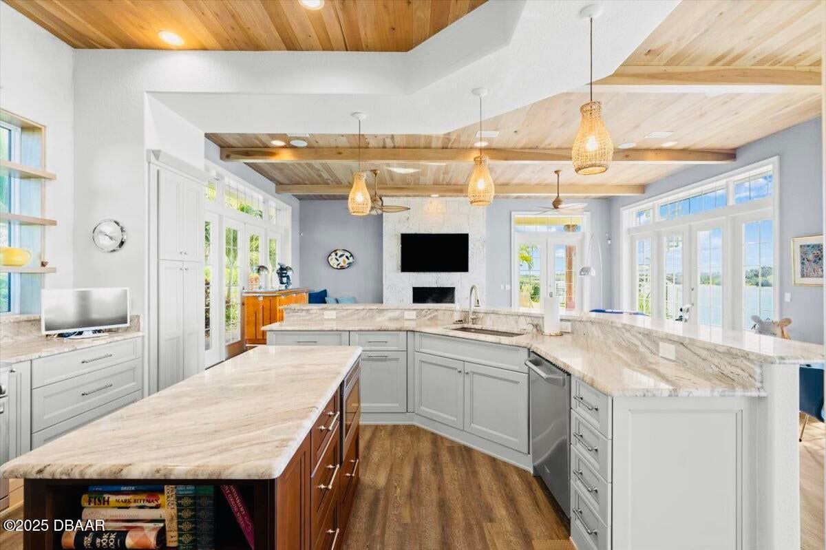 Bright modern kitchen with white cabinets, marble island, wood beams, and pendant lights