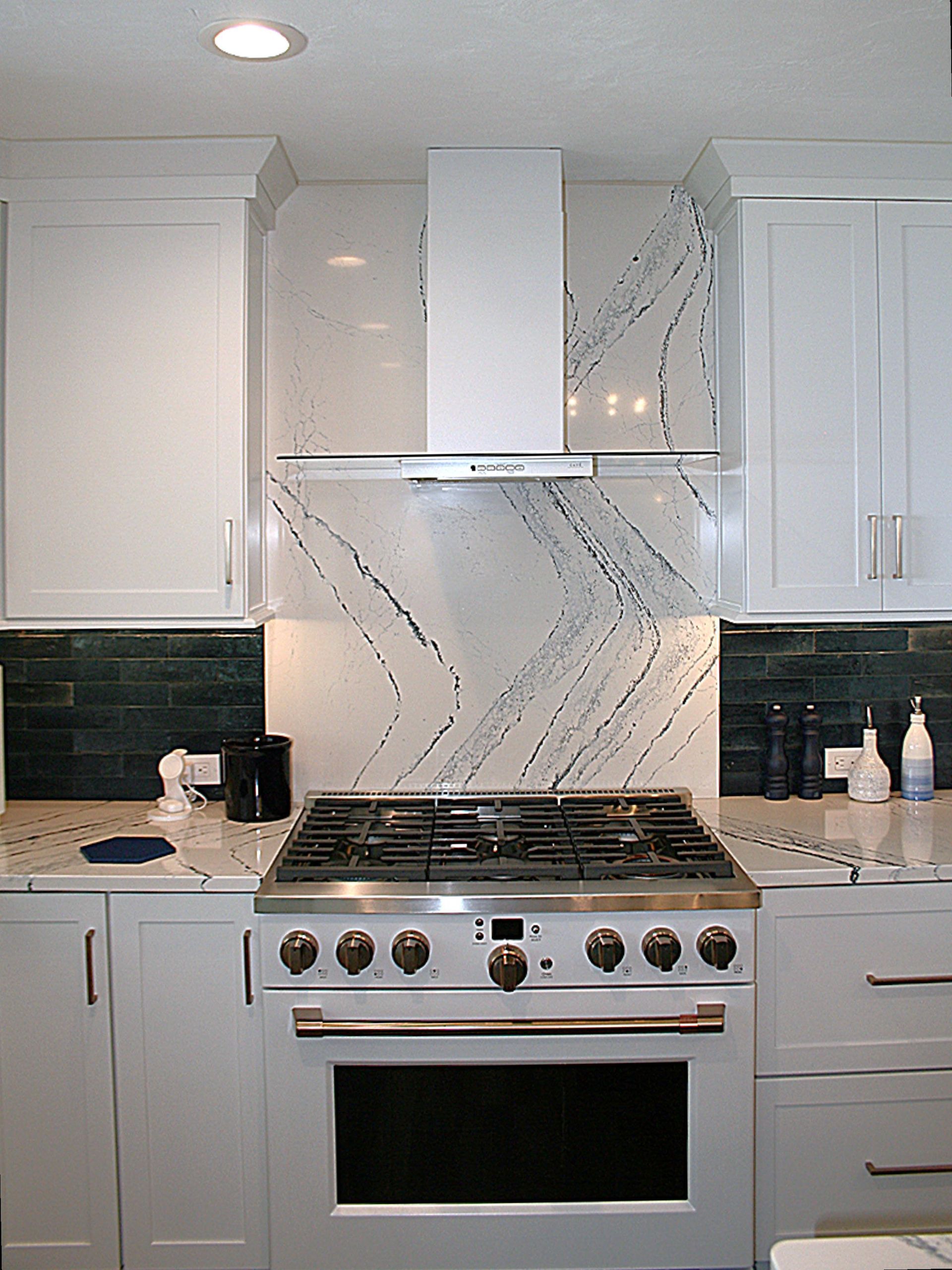 Modern white kitchen with stainless steel stove, range hood, and marble-pattern backsplash