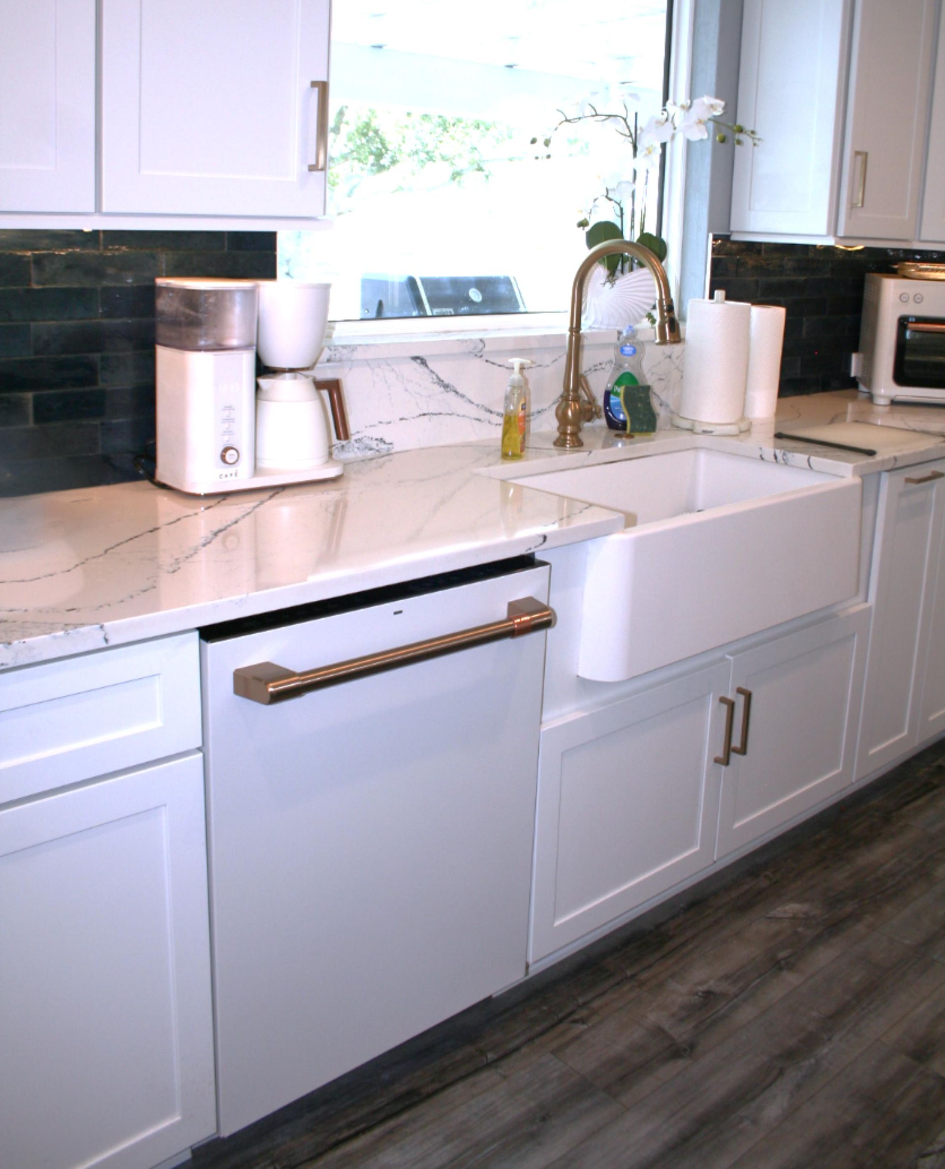 Modern white kitchen sink area with farmhouse sink, coffee maker, and window above the counter.