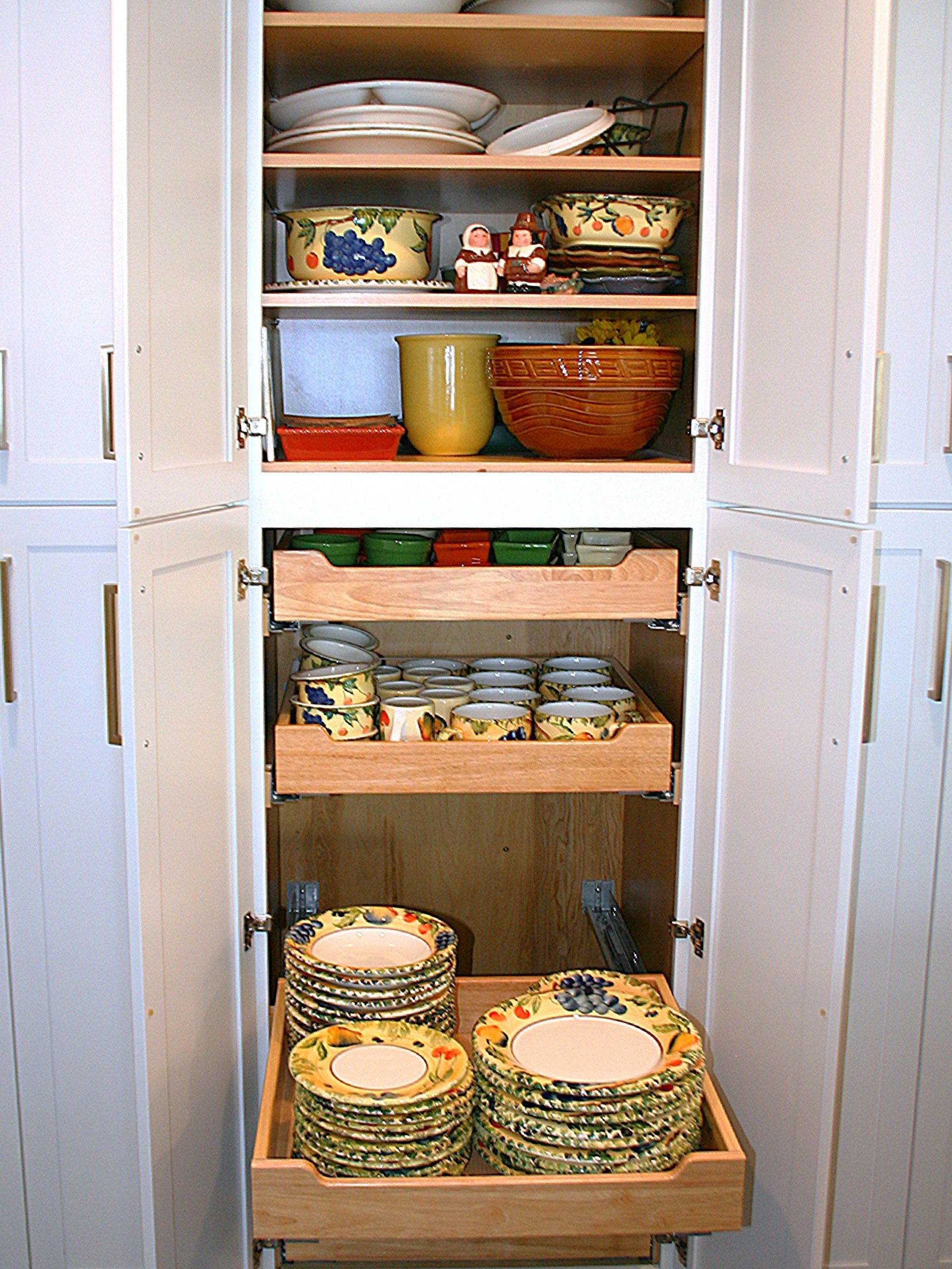 Open pantry with stacked bowls, mugs, baskets, and plates on shelves and a pull-out tray.