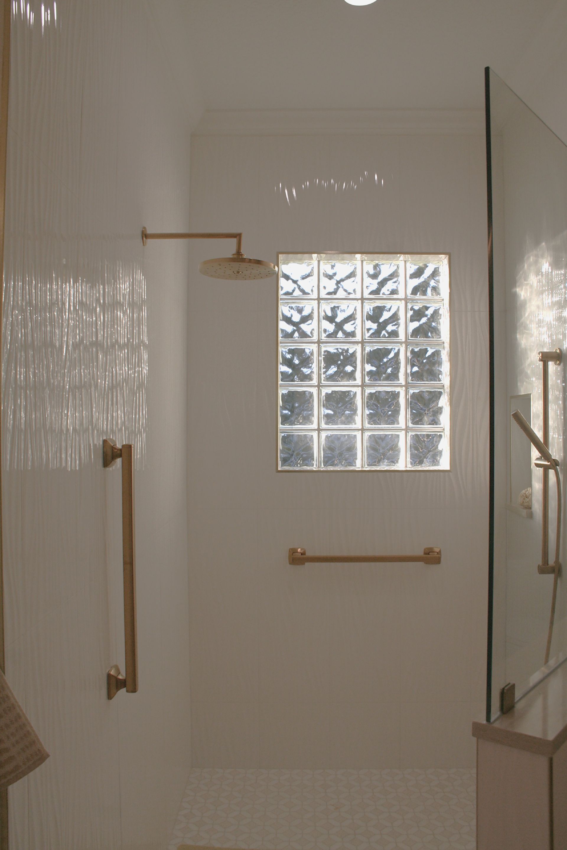White tiled shower with brass rails and a frosted glass block window.