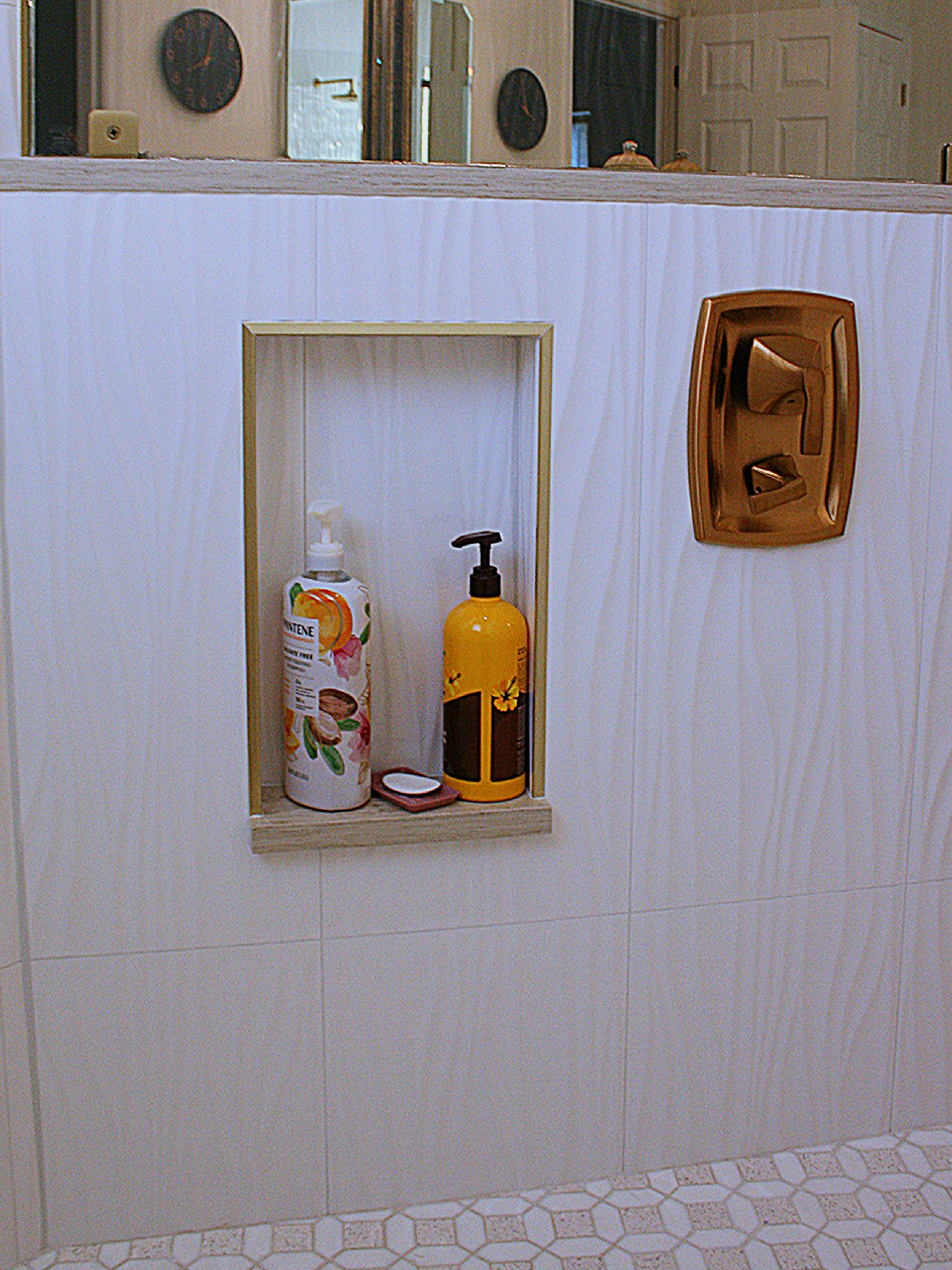 Bathroom wall with recessed shelf holding toiletries and a copper soap dish
