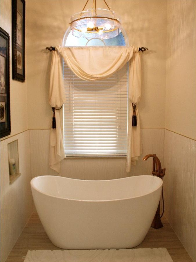 Elegant white bathtub in a narrow bathroom with window blinds and soft blue pendant light