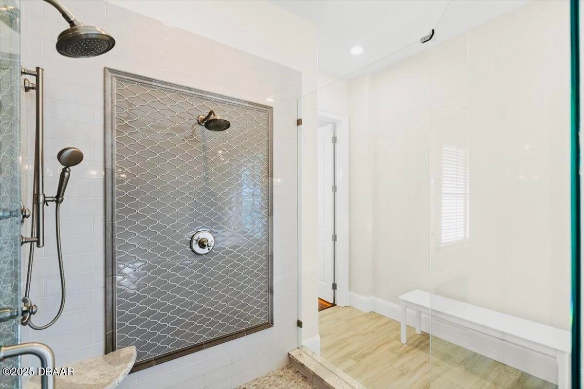 Modern walk-in shower with textured metal door, dark fixtures, and white bench in a bright bathroom