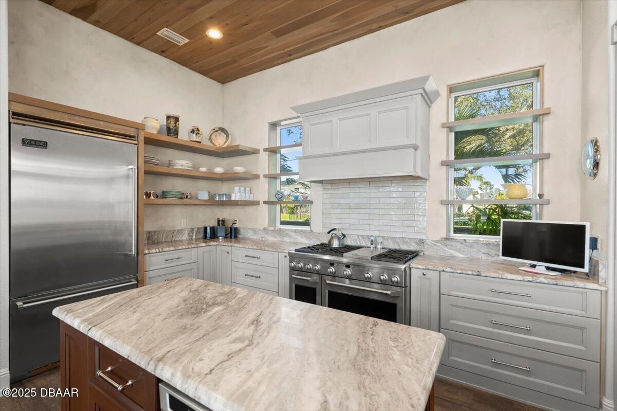 Modern kitchen with marble island, stainless steel appliances, white cabinets, and windows over the stove.
