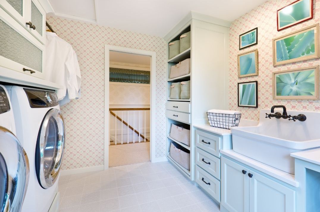 Bright laundry room with washer and dryer, white sink cabinet, and patterned wall art