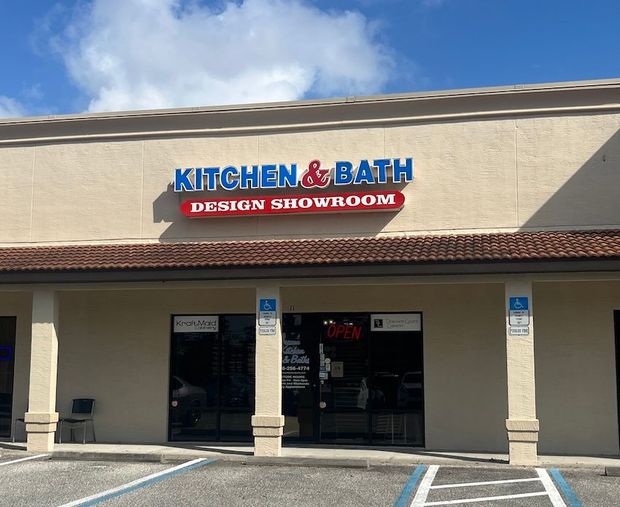 Kitchen & Bath Design Showroom storefront with beige facade and blue-red sign under a cloudy sky