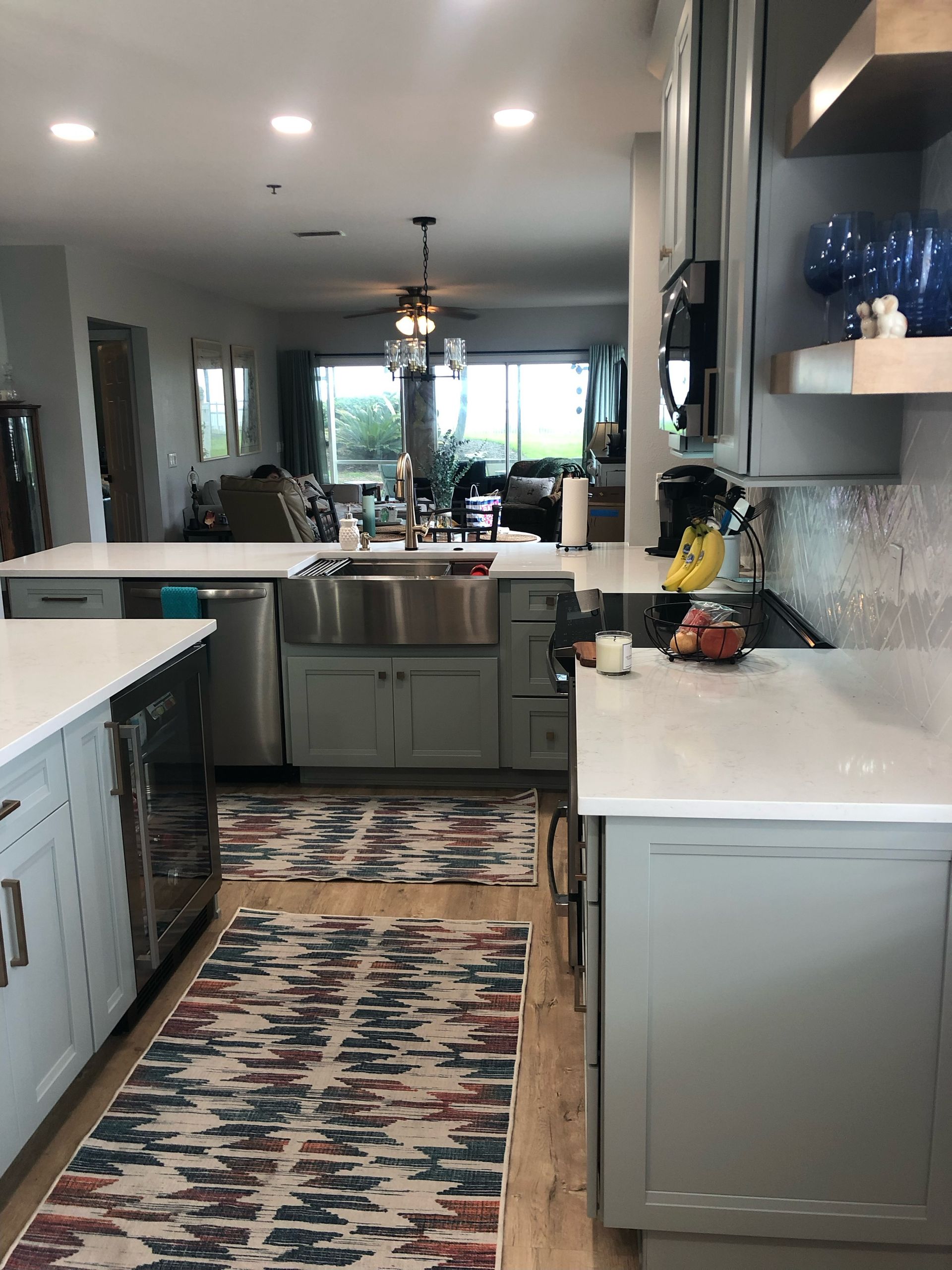 Bright kitchen hallway with gray cabinets, white counters, patterned runner rug, and a window-lit dining area beyond