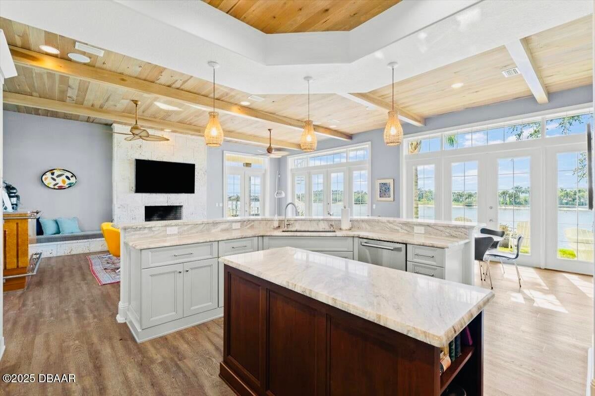 Bright open kitchen with white cabinets, marble island, wood ceiling beams, and large windows.