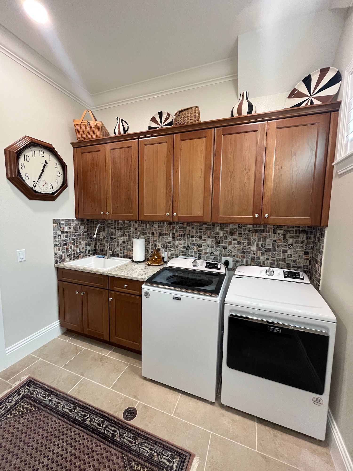 Kitchen with wooden cabinets, mosaic backsplash, white stove, and gray dishwasher under a wall clock.