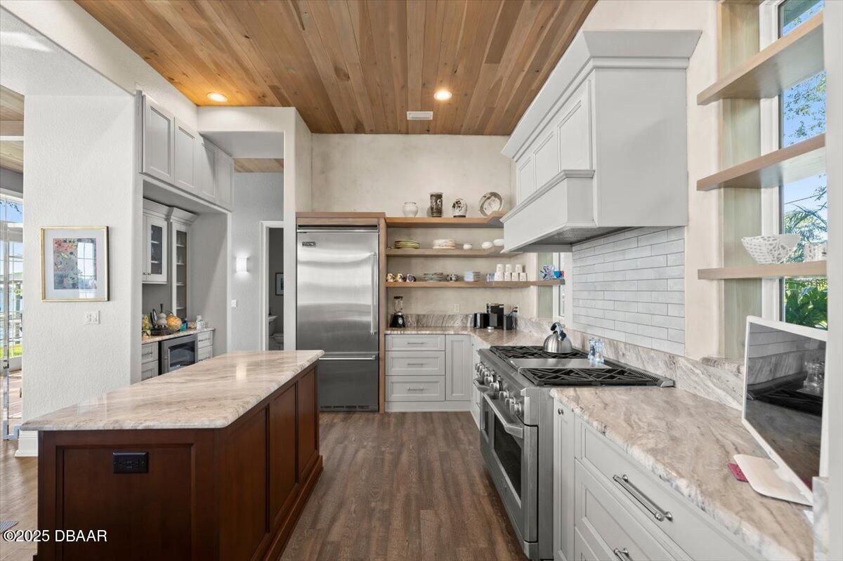 Bright modern kitchen with wood ceiling, marble island, stainless fridge, and open shelving