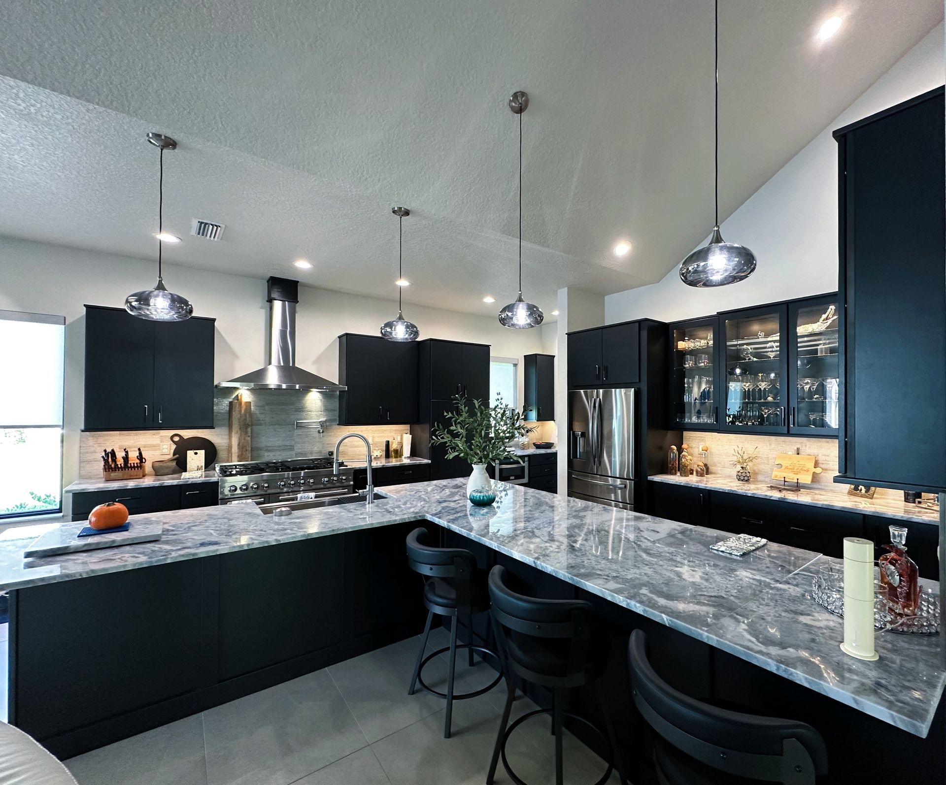 Modern kitchen with black cabinets, marble island, pendant lights, and bar stools under a vaulted ceiling