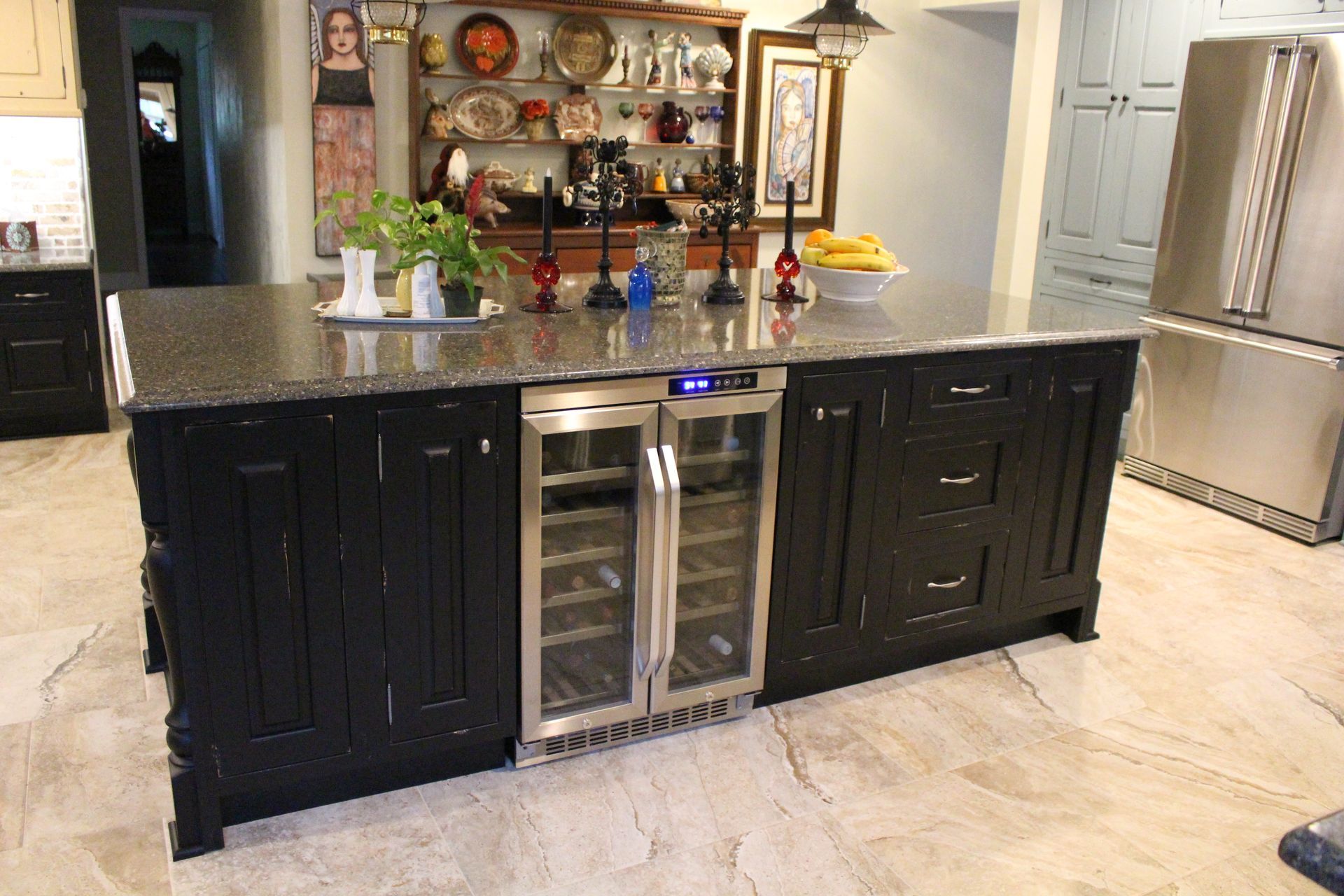 Modern kitchen island with black cabinets, wine fridge, and granite countertop in a bright tiled kitchen
