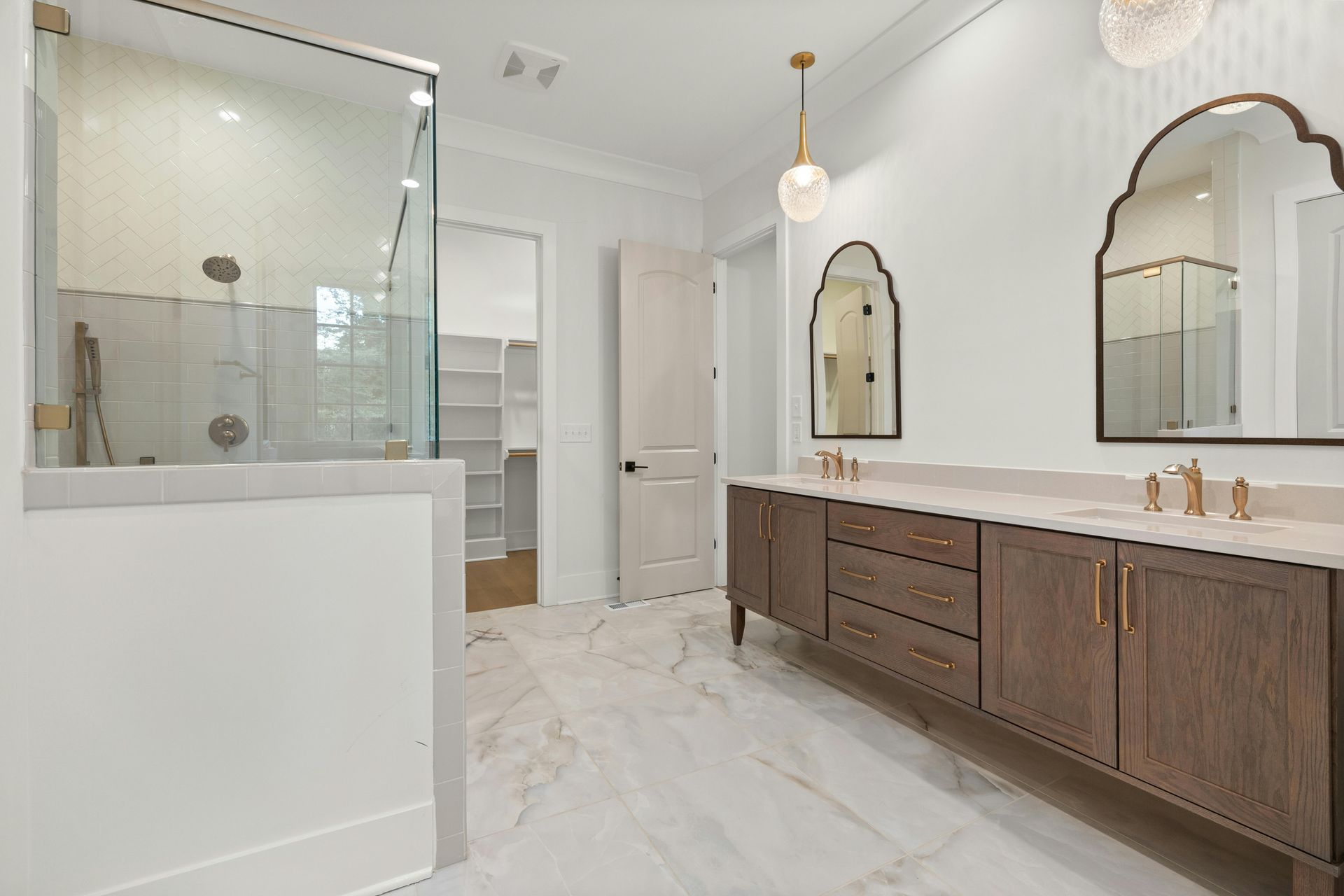 Bright modern bathroom with double vanity, large mirrors, glass shower, and white marble floor.