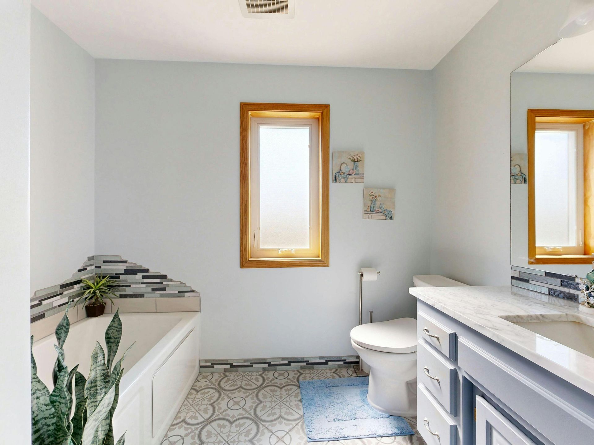 Bright bathroom with white tub, toilet, vanity, and light blue walls, seen from the doorway.