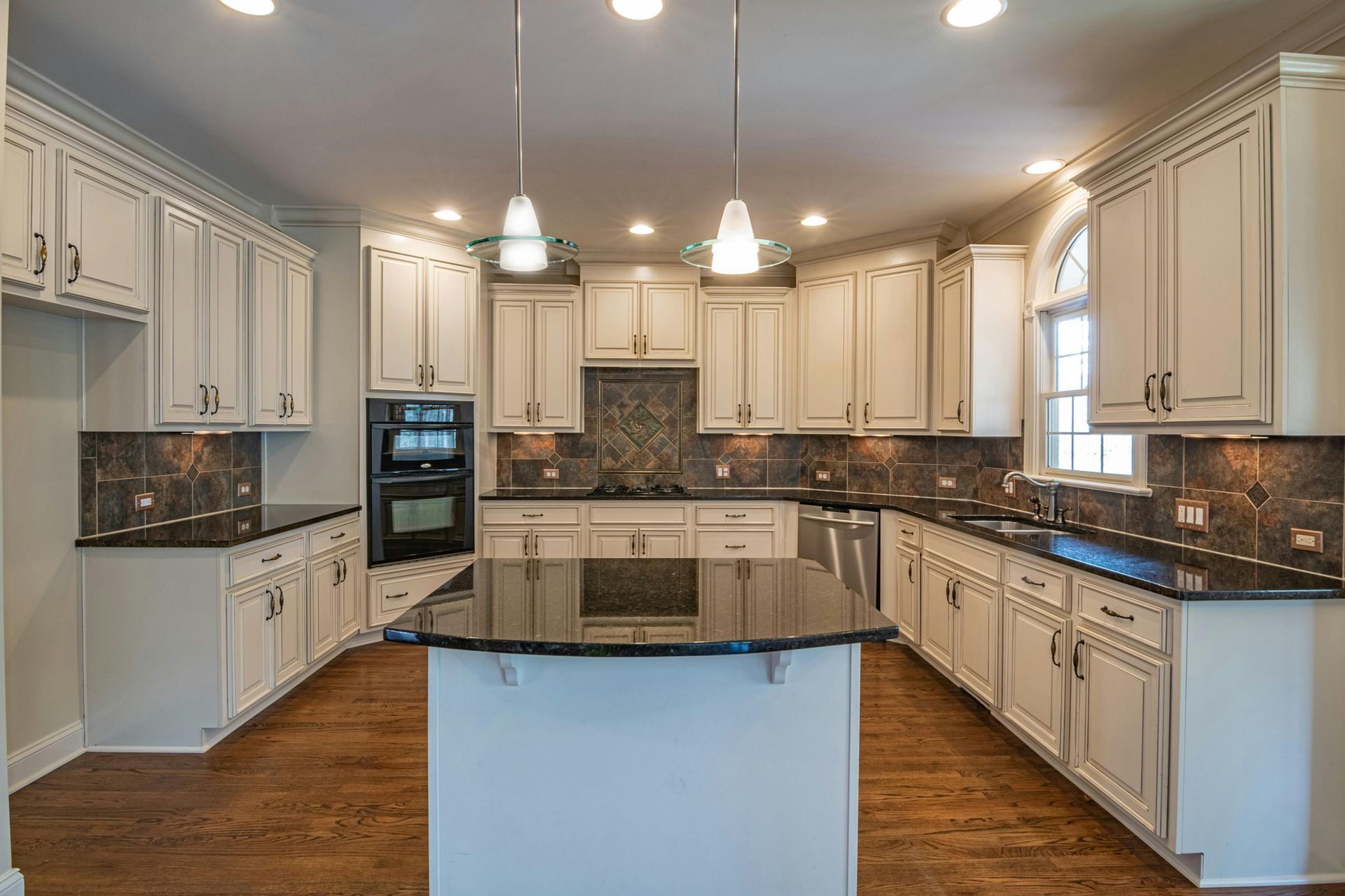 White kitchen with dark countertops, cabinets, and a central island. Hardwood floor.