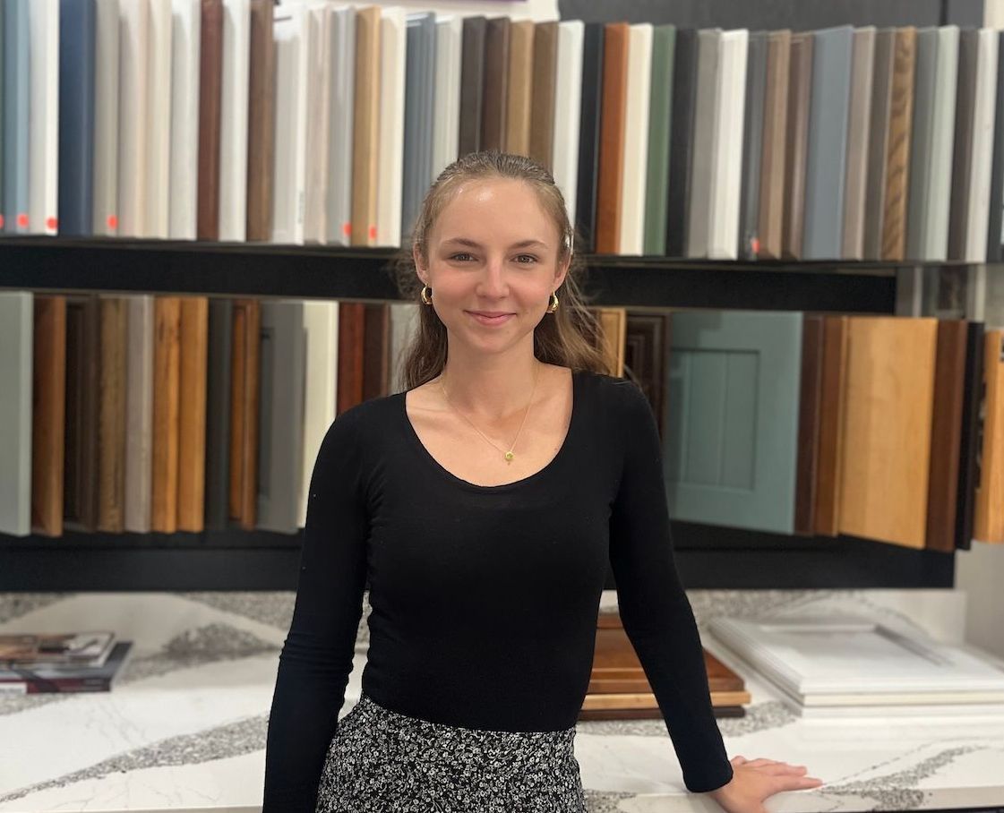 Woman standing in a showroom with rows of colorful samples displayed behind her.