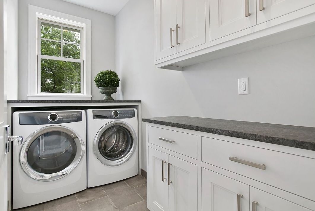 Bright laundry room with front-loading washer and dryer, white cabinets, and a window sill plant