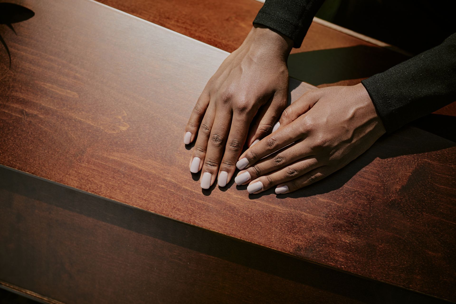 People placing hands on a closed black coffin, funeral flowers present. People placing hands on a closed black coffin, funeral flowers present.