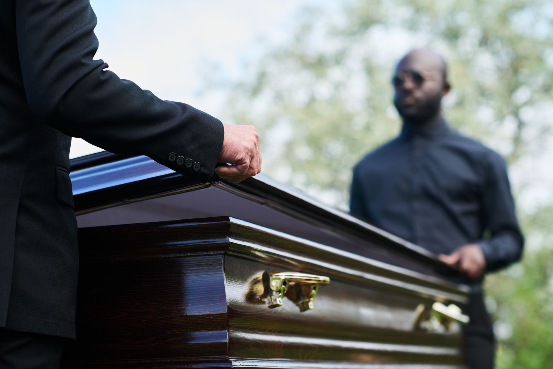 Woman placing flowers on casket, man's arm around her. Funeral, outdoors, with floral arrangements. Woman placing flowers on casket, man's arm around her. Funeral, outdoors, with floral arrangements.