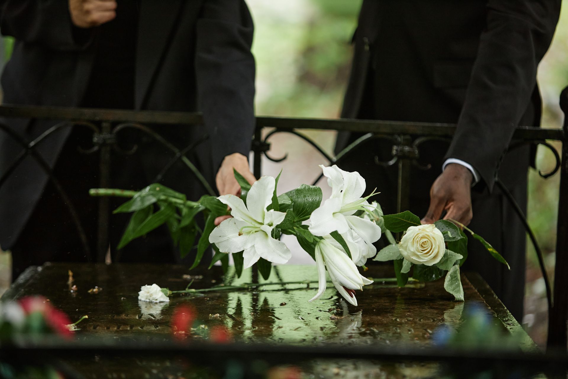 Couple in black clothes mourns, with white lilies on a dark surface, outdoors. Couple in black clothes mourns, with white lilies on a dark surface, outdoors.
