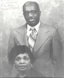 Couple in formal attire, the man standing behind the seated woman, both wearing glasses. Couple in formal attire, the man standing behind the seated woman, both wearing glasses.