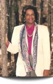 Woman in white blazer, holding a tree. Wearing scarf, pink shirt, necklace. Outdoor setting. Woman in white blazer, holding a tree. Wearing scarf, pink shirt, necklace. Outdoor setting.