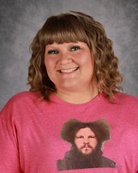 Smiling person in a pink shirt with a face graphic, standing against a gray studio backdrop