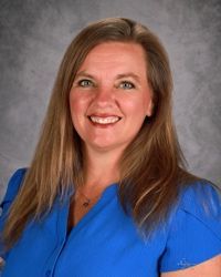 Smiling woman in a blue blouse against a gray studio backdrop