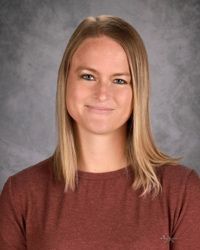 Portrait of a person with straight blond hair wearing a maroon shirt against a gray backdrop
