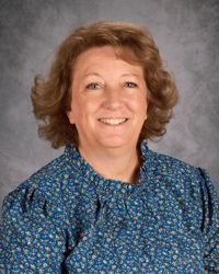 Smiling woman in a blue patterned blouse against a gray studio background