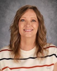 Smiling person with wavy brown hair wearing a white sweater with red and black stripes against a gray backdrop