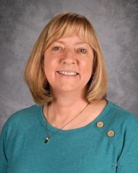 Studio portrait of a smiling woman in a teal top against a gray backdrop