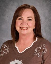 Smiling woman in a brown floral top against a gray studio backdrop