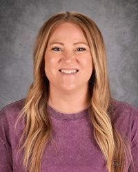 Smiling woman in a purple shirt against a gray studio backdrop