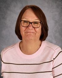 Portrait of a person wearing glasses and a light pink sweater against a gray backdrop