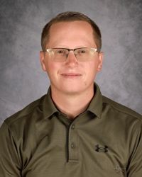Portrait of a man wearing glasses and an olive polo shirt against a gray studio backdrop