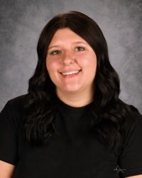 Smiling person with long dark hair wearing a black top against a gray studio backdrop