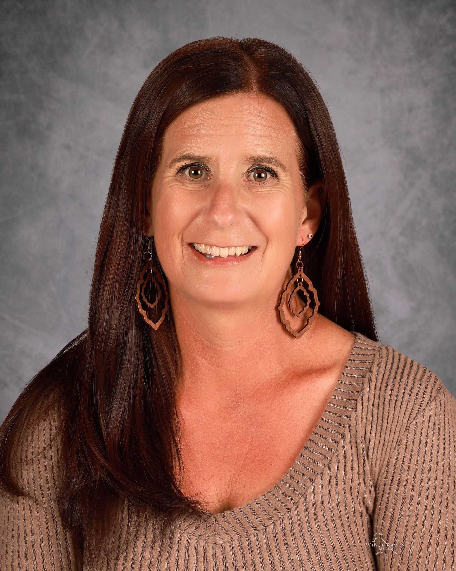 Smiling woman with long brown hair wearing a beige sweater against a gray studio backdrop