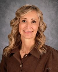 Smiling woman in brown blouse with wavy blonde hair against a gray studio background