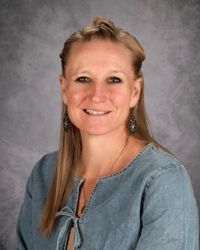 Studio portrait of a smiling person in a blue blouse against a gray backdrop