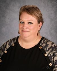 Portrait of a woman in a black top and patterned cardigan against a gray studio backdrop